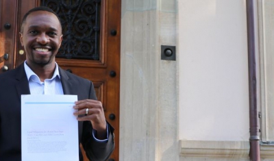 Joshua Niyo holding his paper in front of the Geneva Academy