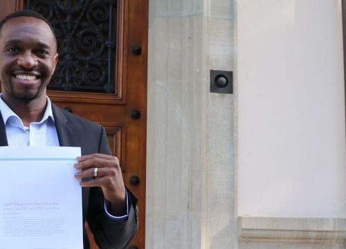 Joshua Niyo holding his paper in front of the Geneva Academy