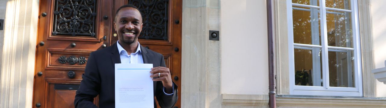 Joshua Niyo holding his paper in front of the Geneva Academy