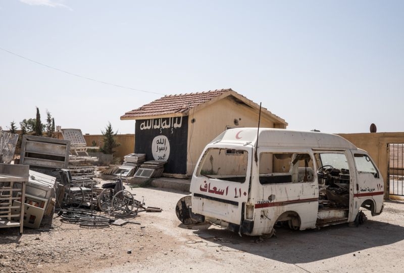 Abandonned ambulance on the Taqba hospital parking. In the background the ISIS flag was painted on a wall. The city was taken control end of April by the Syrian Democratic Army, an Kuridish-Arabo alliance support by the international coalition. During the fight, the ISIS fighters were taking refuge inside.